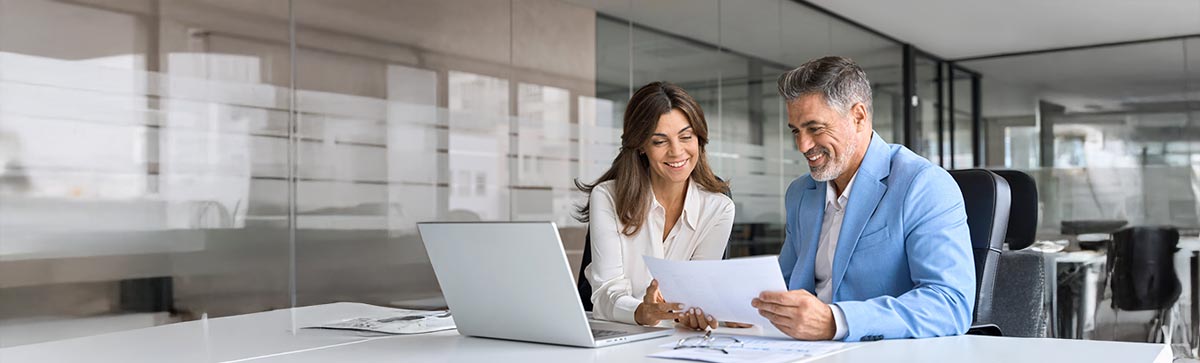 Freundlicher Vertriebsmitarbeiter sitzt an einem Schreibtisch im modernen Büro mit einem Bildschirm im Hintergrund, der Energiedaten zeigt.
