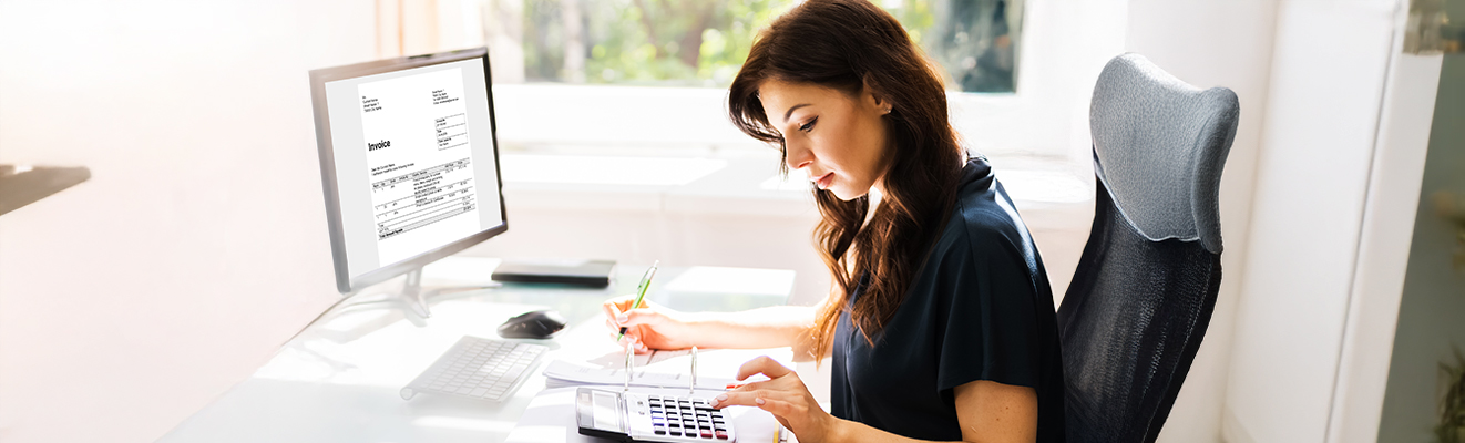 Freundlicher Mitarbeiter sitzt an einem Schreibtisch im modernen Büro mit einem Bildschirm im Hintergrund, der Energiedaten zeigt.