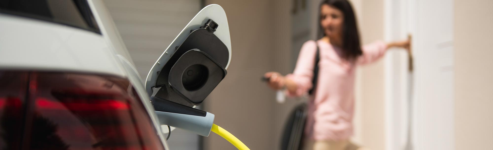 Eine Frau und ein Auto, welches gerade mit einem Stromkabel verbunden ist